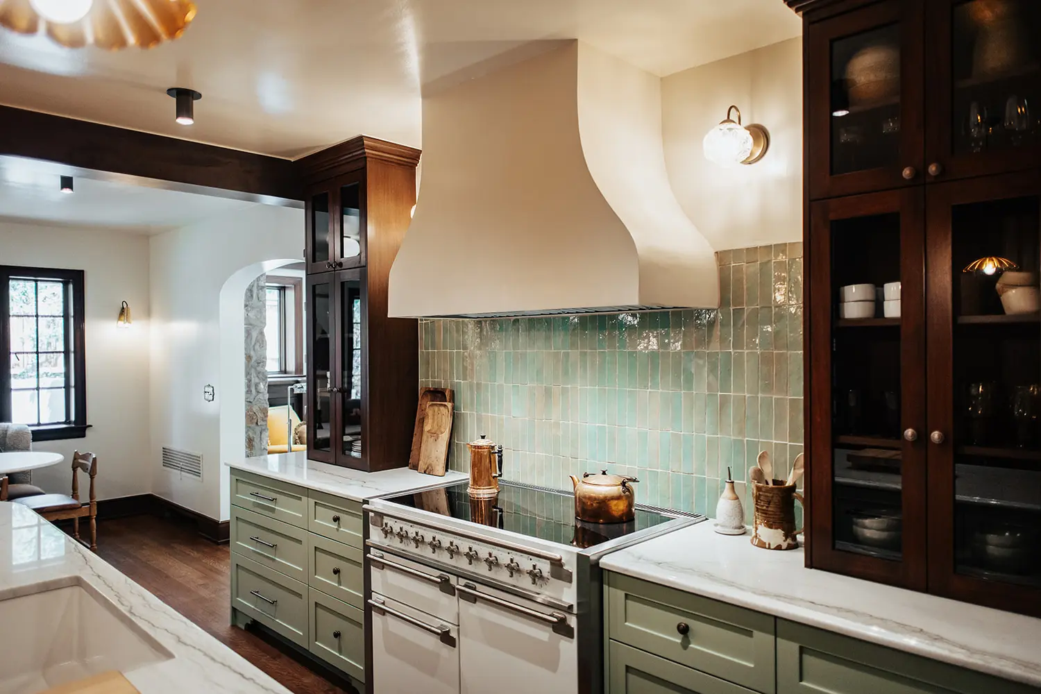 Custom plaster range hood, sage green tile backsplash, and glass display cabinetry in a luxury Utah kitchen