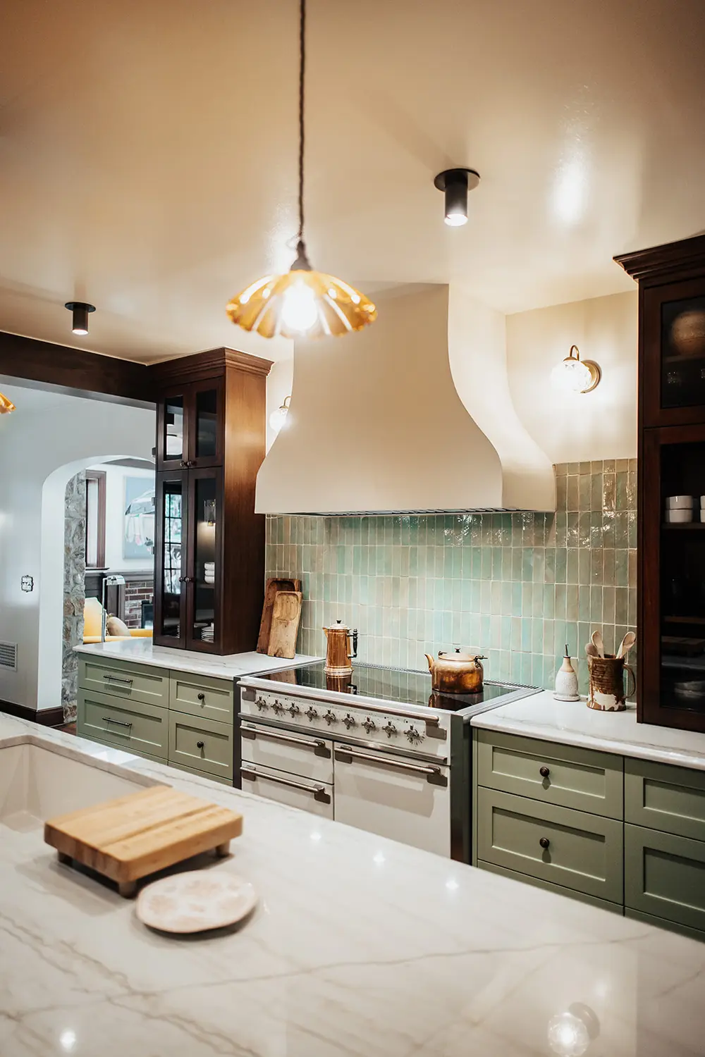 Range wall with sage green tile, copper cookware, and brass fixtures in a custom Utah kitchen